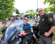 Image of a boy on a Sheriff's Office motorcyle, with a deputy smiling