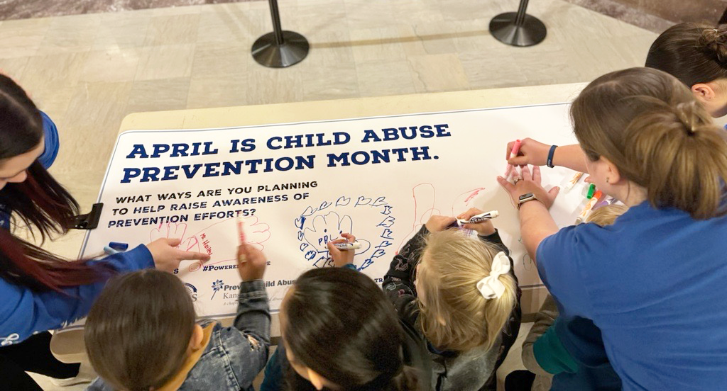 Photo of children and adults drawing on an "April is Child Abuse Prevention Month banner"