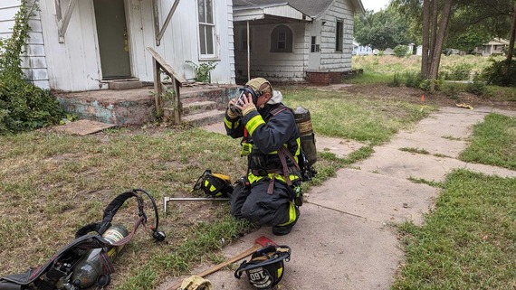 Acquired structure training - firefighter kneeling in front of house adjusting his face mask 