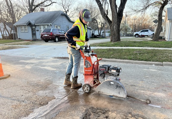 Street worker cutting pavement with saw