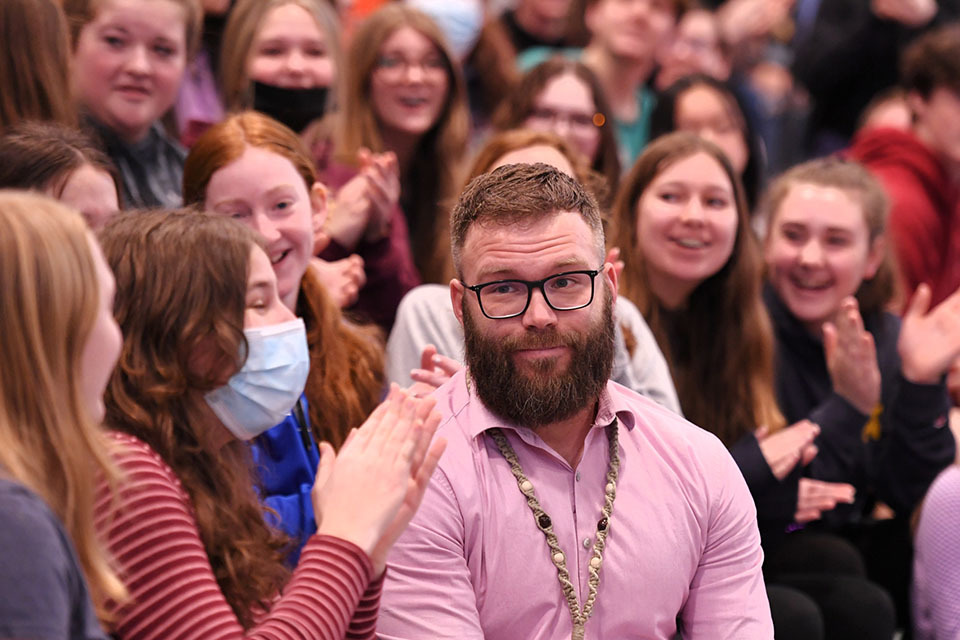 Picture of a man looking surprised, surrounded on by students clapping and smiling.