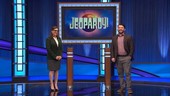 A woman and a man standing in front of a large screen that reads: Jeopardy!