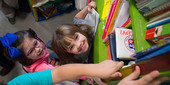 Picture of several small children reaching for books on a shelf and smiling.