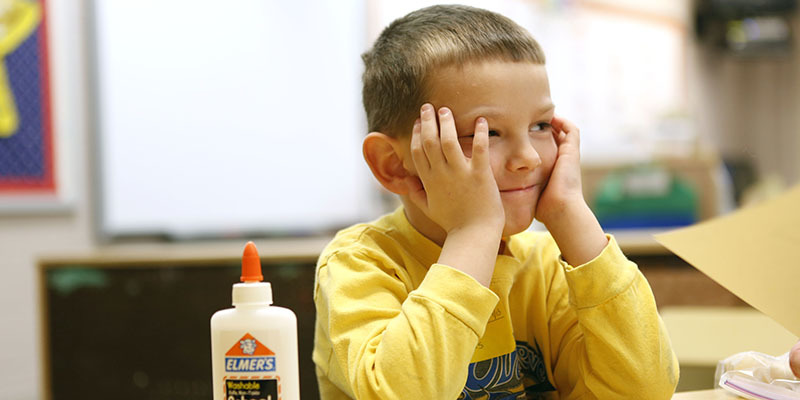 Picture of a smiling boy with his head resting on his hands.