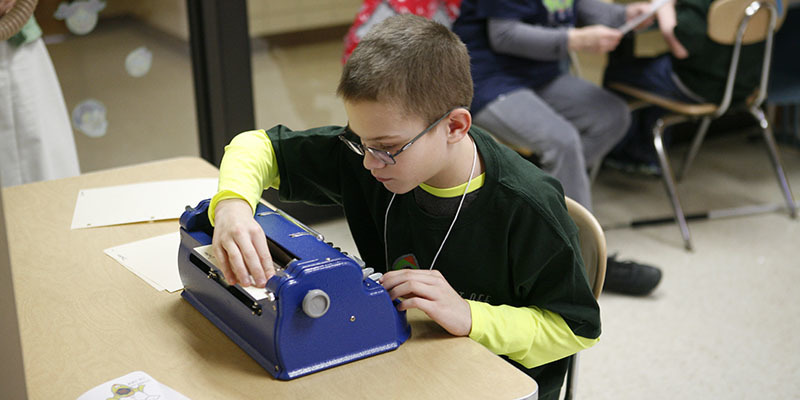 Picture of a young boy reading text he has written using a Braille typewriter.