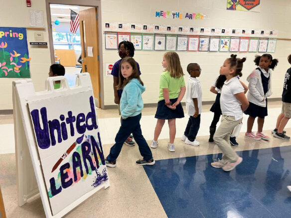 Students walk through a hallway past a sign that reads: "United We Learn."