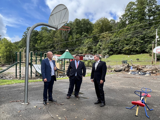 Three men stand on a damaged basketball court in front of debris and a damaged playground.