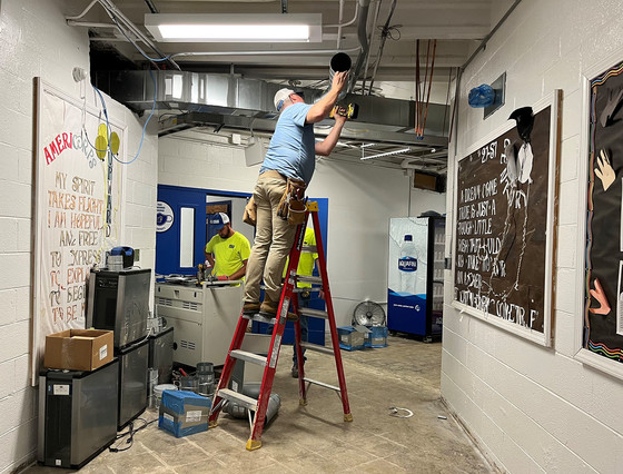 A picture of two men working on air conditioning ducts in a school hallway.