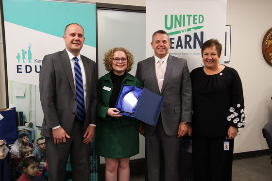 A picture of Audrie Gilbert holding a glass trophy. Standing beside her are Kevin C. Brown, Jason E. Glass and Lu S. Young.