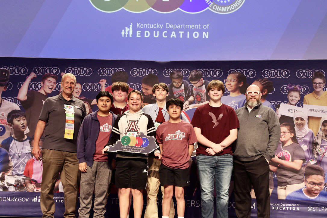 Picture of a group of six students on stage holding an STLP trophy standing beside two Kentucky Department of Education staff members.