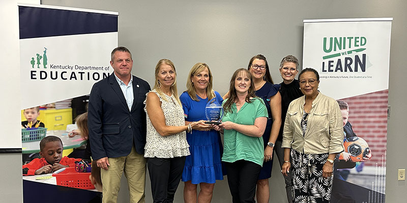 Jason E. Glass and Sharon Porter Robinson stand with a group of five smiling women who are holding onto a glass trophy.