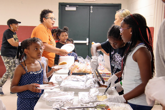 Adults serve kids food from prepared trays on a table