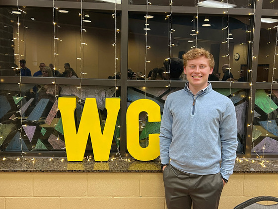 A man stands in front of a window that has the letters "WC" in gold on it.