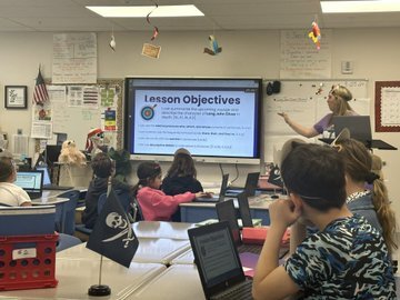 Teacher in front of classroom with Lesson Objectives on the board