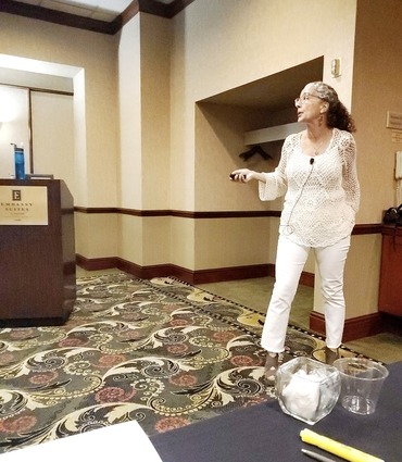 A woman in a white shirt and pants addresses an audience