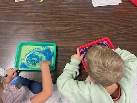 Students tracing letters in sand trays