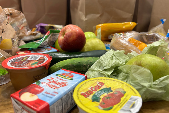 A pile of food, including a dipping container of salsa, a box of apple juice and various fruits and vegetables