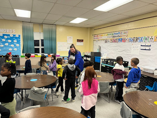 Young children stand in pairs around a classroom participating in a hand-clapping activity. 
