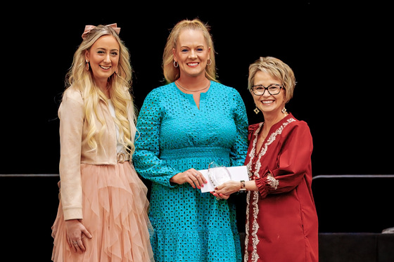 Three women pose for a photo as the woman in the middle holds a glass award