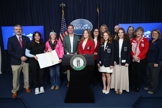 Group of students and KDE staff stand at a podium with the Kentucky Governor, Andy Beshear, during a proclamation signing for CTE month