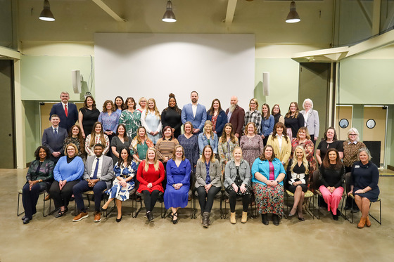 A group of a few dozen people arranged in seated rows pose for a photo in an auditorium