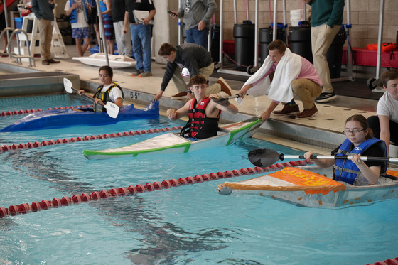 Students in homemade kayaks in an indoor pool