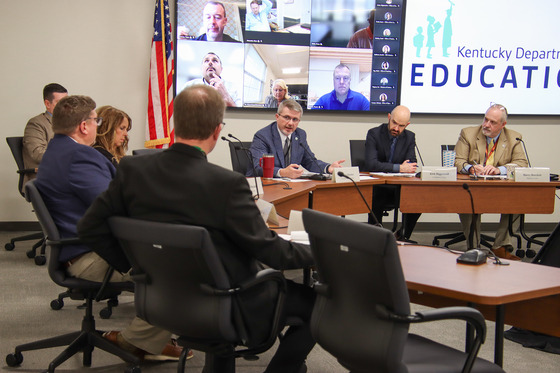 group of individuals sitting around a large table having discussions. 