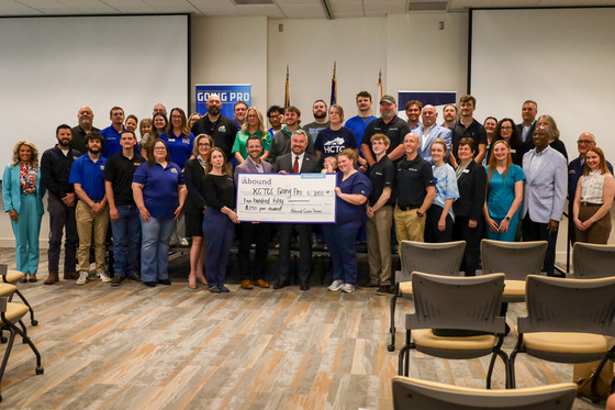 A group of dozens of people pose with a few people in the middle holding a giant check