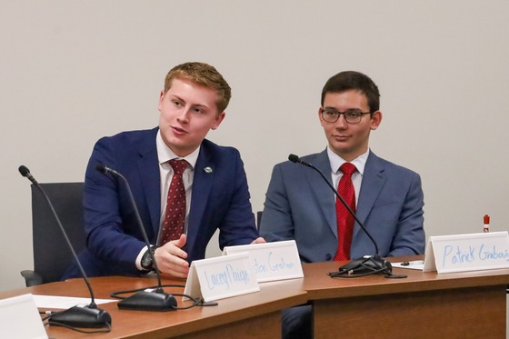 Two students sitting at a table with their attention toward a presenter.