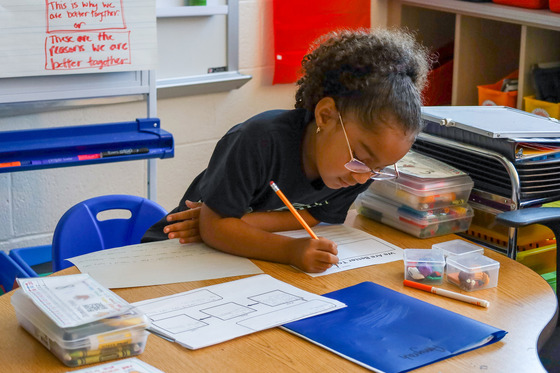 A student sits at a desk with a pencil working on an assignment