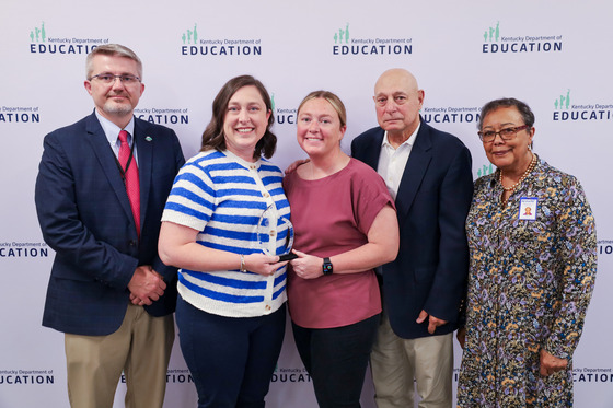 five people standing in front of a background being presented an award.