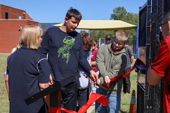 A group of kids cut a red ribbon near a metal gate