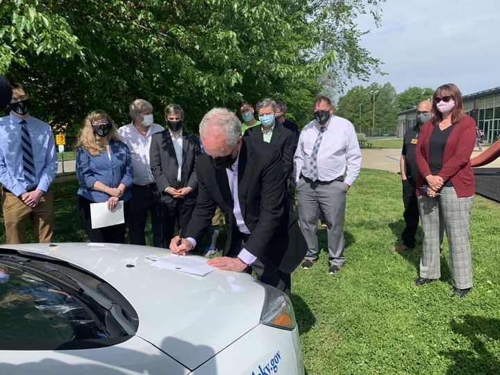 Mayor Fischer signing executive order on the hood of a Louisville Metro EV