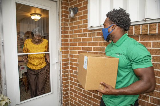 A box of meals is delivered to an elderly woman at her front door by a young man