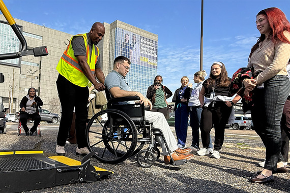 Student sits in wheelchair and boards paratransit vehicle.