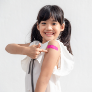 School age girl smiling and pointing at a vaccine bandage on her arm