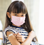 Child wearing a mask and pointing to bandaid 