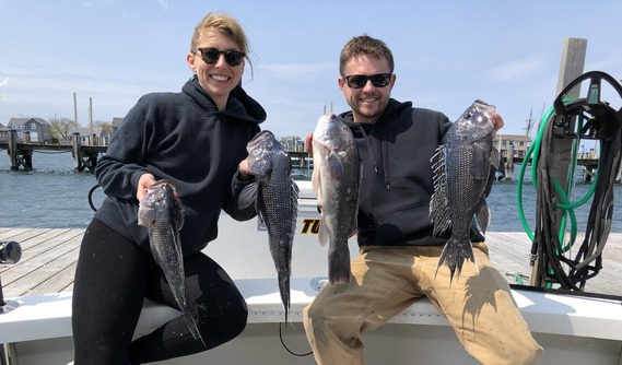 Two anglers holding up their catch on a dock.