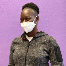 A middle-aged black woman with a puff ball smiles underneath a face mask