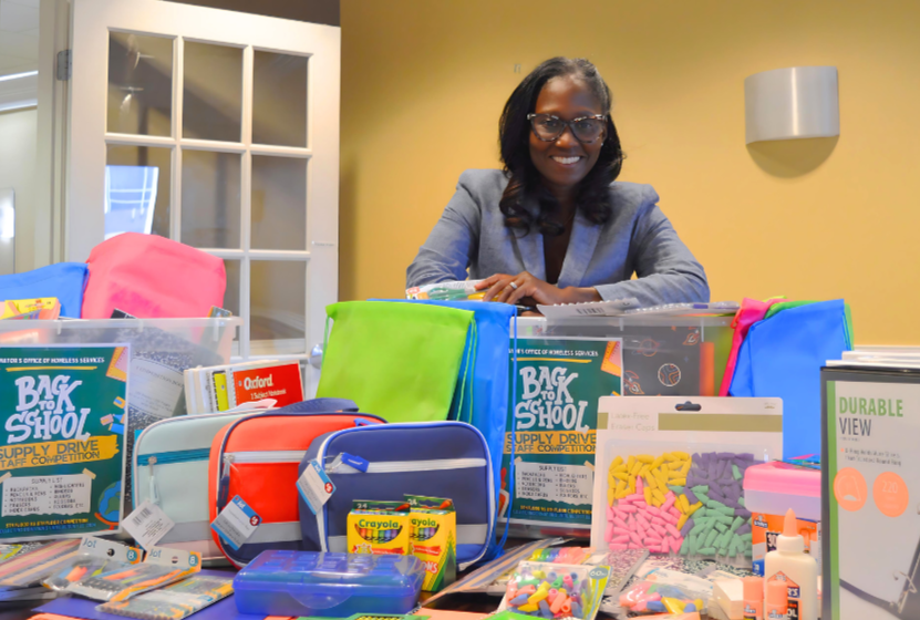 Director Simmons stands in a conference room with a table full of school supplies donated by the MOHS staff.