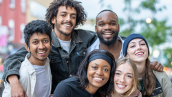 A group of six diverse young adults huddled closely together for a group portrait