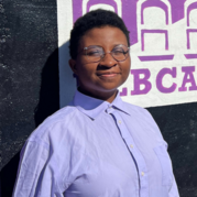 A young adult female wearing circular glasses and a lilac button up shirt