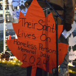 A large orange cut-out leaf that reads "Their Spirit Lives On. Homeless Persons' Memorial Day 2024"