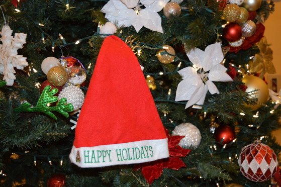 A Santa Claus hat with Happy Holidays hangs on a tree