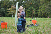 Photo of two children standing next to newly planted tree seedling