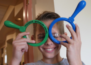 A child holds two magnifying lenses over his eyes like their glasses