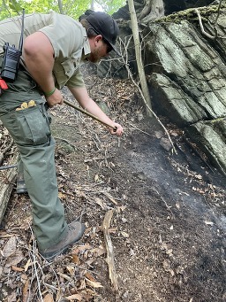 A ranger spraying water on a smoldering fire