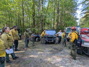 A burn crew listens to a safety briefing and goes over the prescribed burn plan at the staging area.