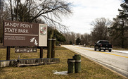 Cars driving past entrance sign for Sandy Point State Park