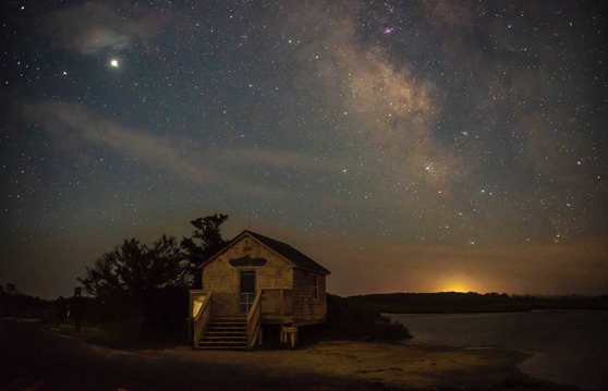 Starry night sky above a building with the bay in the background